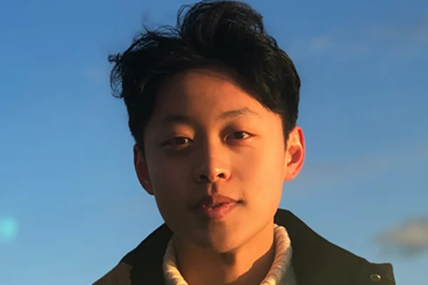 A young man with dark hair wearing a white sweater, smiling and looking directly at the camera.