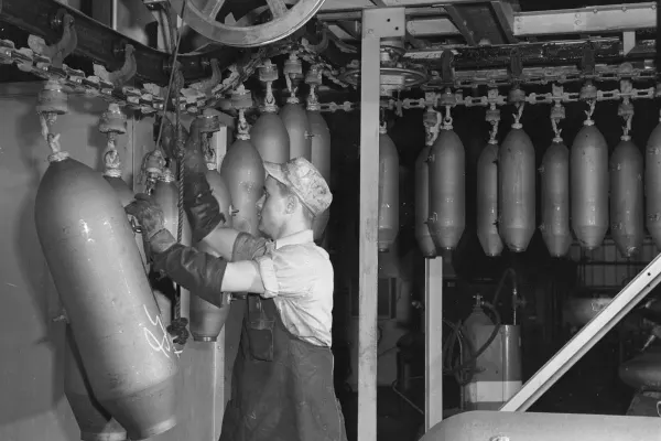 Factory worker secures bomb casings to an overhead conveyor line in an assembly plant.