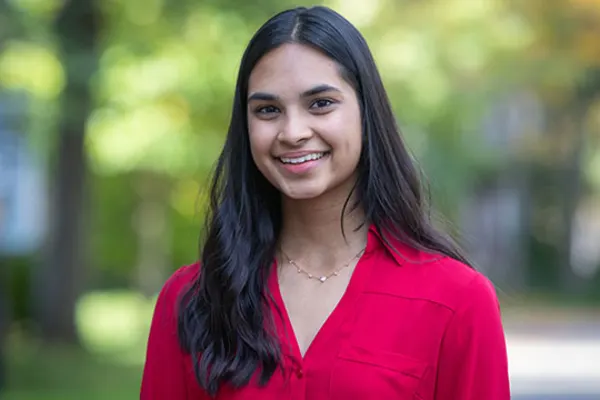 A young woman in a red shirt smiles warmly at the camera, exuding a cheerful and friendly demeanor.