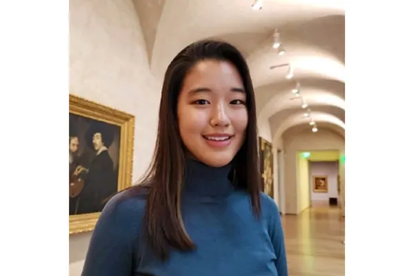 A young woman smiles while standing in an art museum, surrounded by colorful artwork and exhibits.