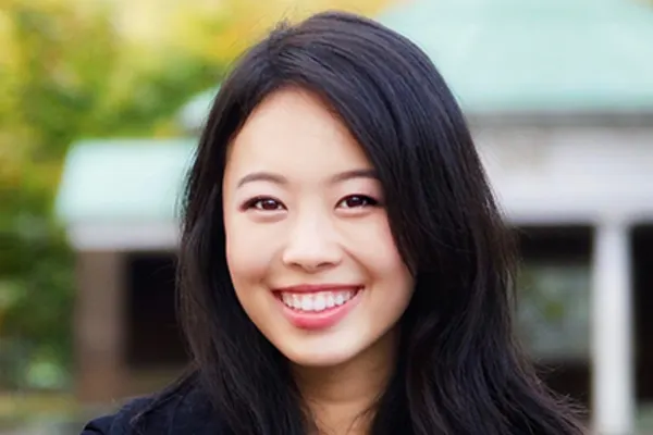 A woman with long black hair smiles warmly at the camera, exuding a friendly and approachable demeanor.