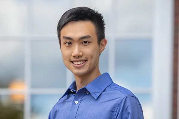 A young man in a blue shirt smiles warmly at the camera.