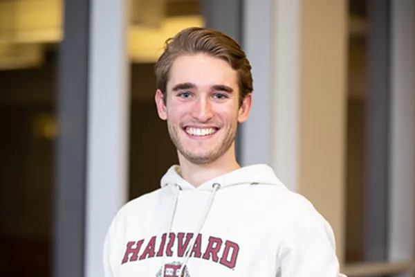 A young man wearing a white sweatshirt smiles warmly at the camera.