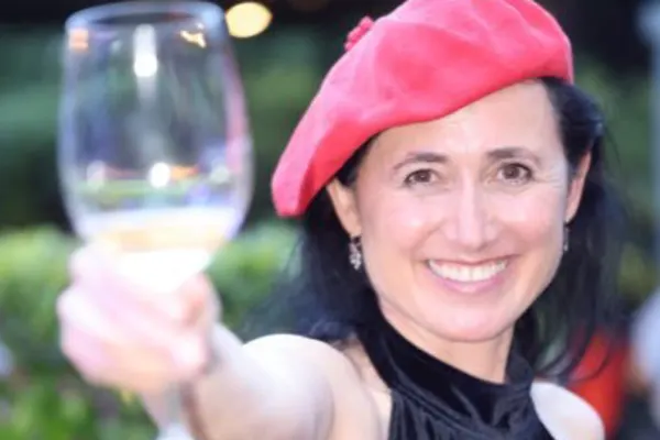 Smiling person in a pink beret raising a wine glass toward the camera outdoors.