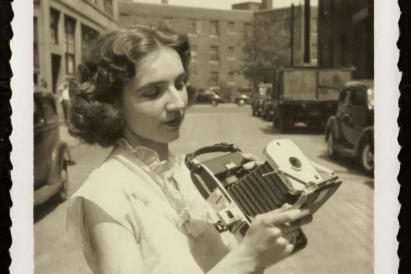 Woman standing outside Polaroid building holding camera