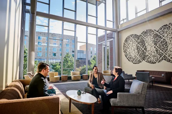 Four people in conversation sitting around a table in the sunlight Chao Center second floor lounge. 