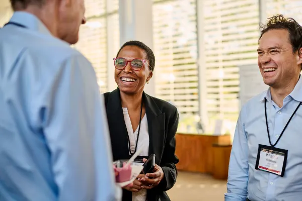 Two male and one female executive participants laugh and talk inside a Harvard Business School building on campus
