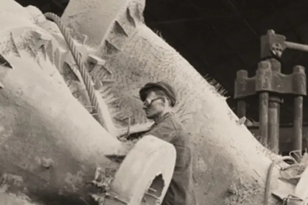 A man in goggles stands amidst a large machine in sepia tones.