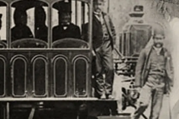 Passengers in a train car with railroad workers standing beside the car in black and white.