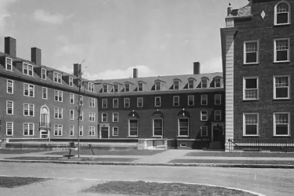 A grassy courtyard in front of the Harvard Business School building is shown in black and white, under a nearly cloudless sky.