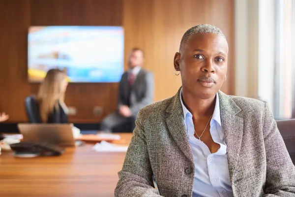 A Black business woman in an office conference room with two professionals engaging in discussion in background