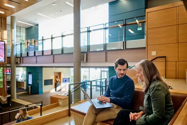 A man and woman engaged in conversation looking at a laptop while inside the HBS Chao Center building.
