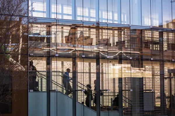 Glass façade of Tata hall building from exterior with people on interior stairs