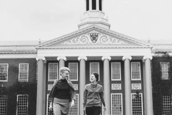 Two women walking across lawn in front of Baker Library
