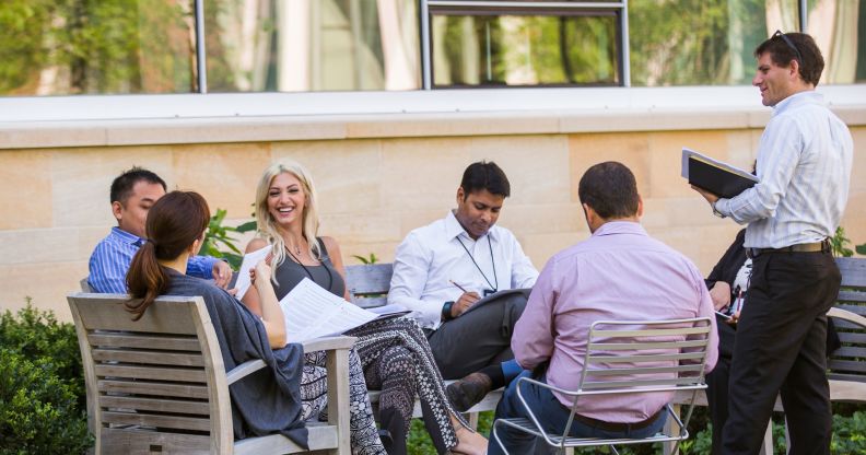 Executives gather around a table outside on the Harvard Business School campus to have a conersation