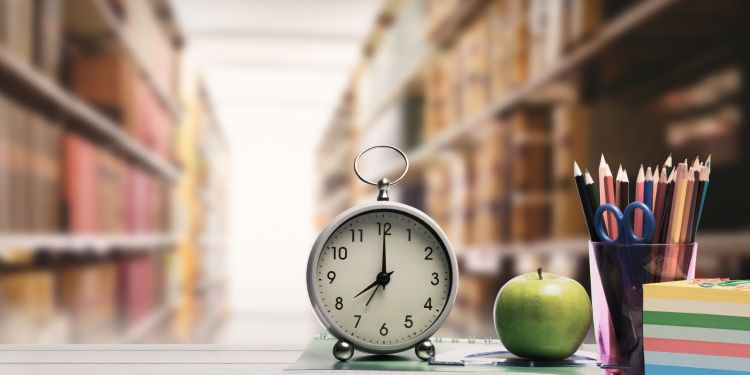 Clock sitting next to an apple and pencils in a library