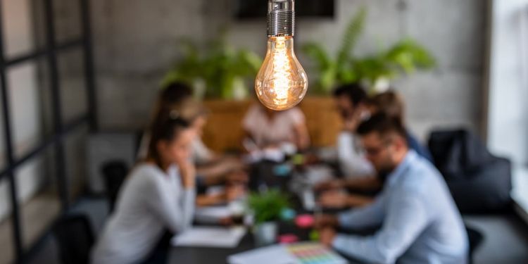 Co-workers strategizing together at a table with a lightbulb lit up over their heads.