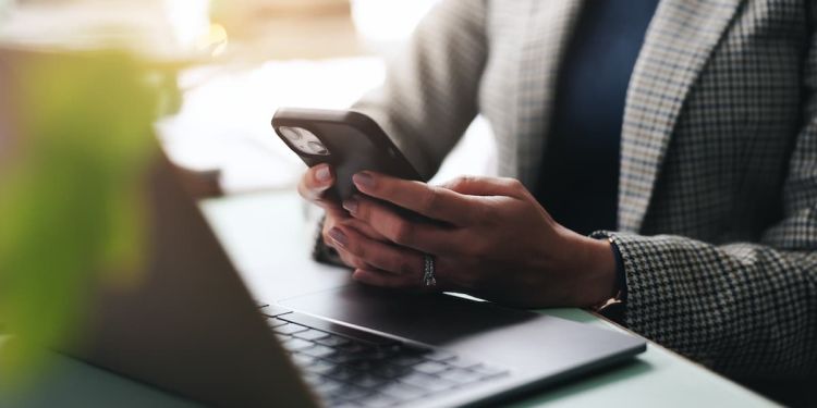 A woman on her cell phone, while sitting in front of her laptop.