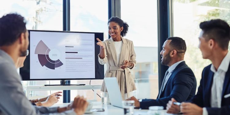 Woman giving a presentation in a meeting. Three business professionals watching the presentation on a screen.