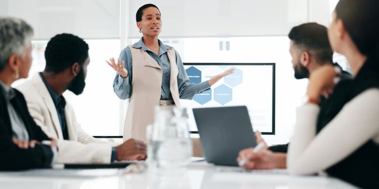 A leader in front of a monitor speaking to their colleagues seated at a conference table