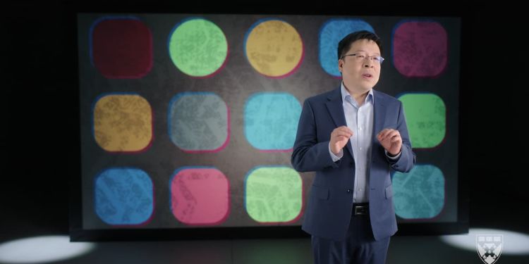 Harvard Business School Professor Feng Zhu speaking in front of a backdrop with multiple multi-colored shapes