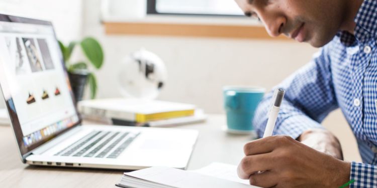 Man taking notes while using laptop