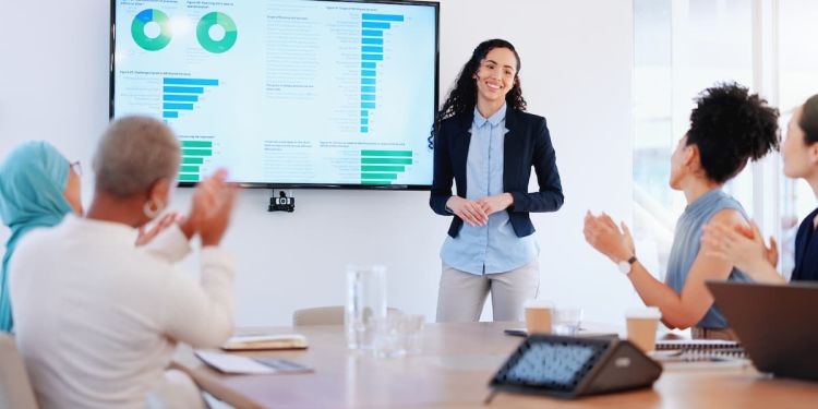 Business leader standing at a monitor displaying a presentation as their team applauds