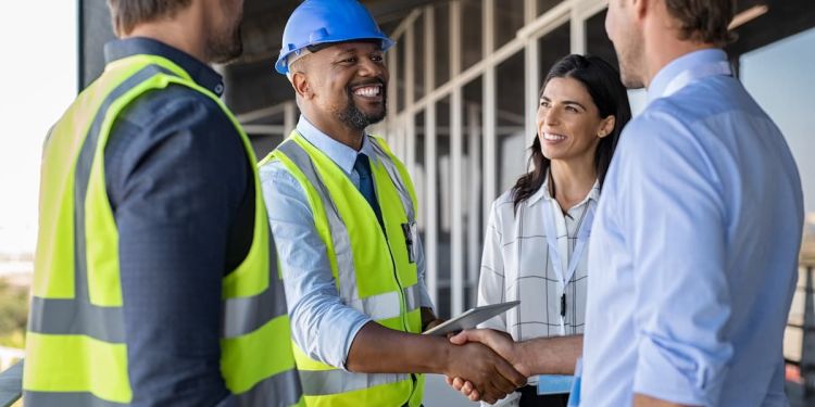 An engineering manager in safety gear shaking hands with colleagues in business attire